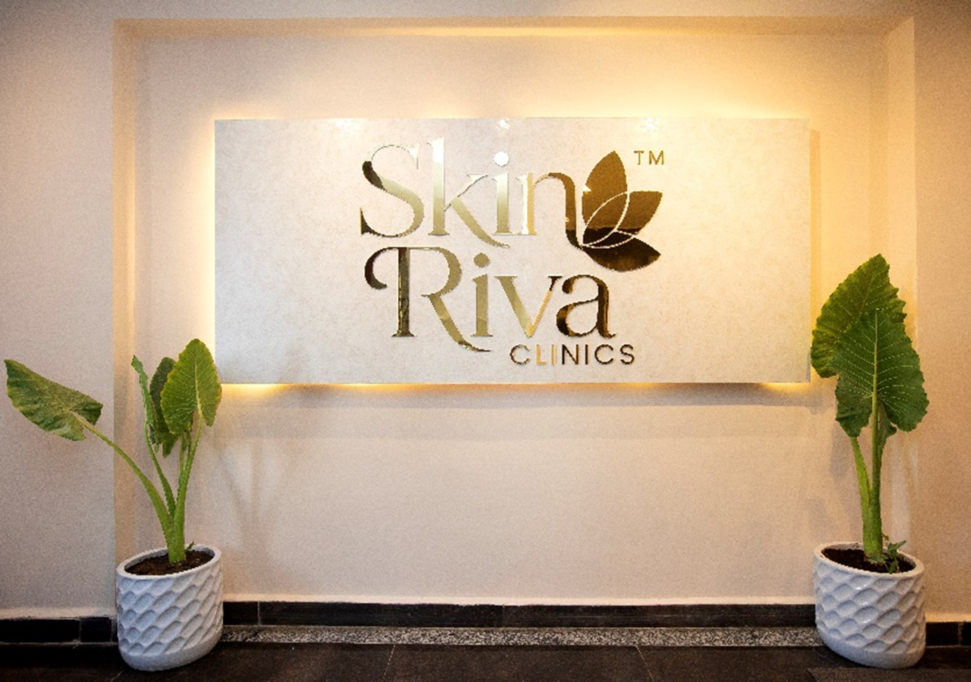 Skin Riva Clinics signature backlit gold logo on marble wall with planters