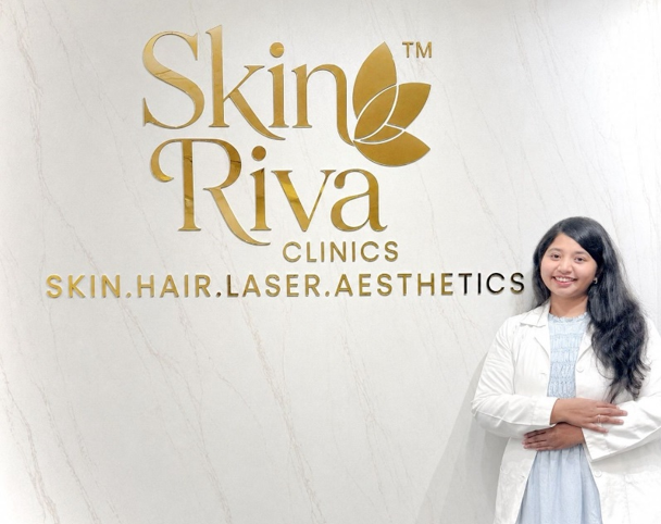 Dr. Sindhura standing in front of the Skin Riva Clinics logo at the Manikonda clinic